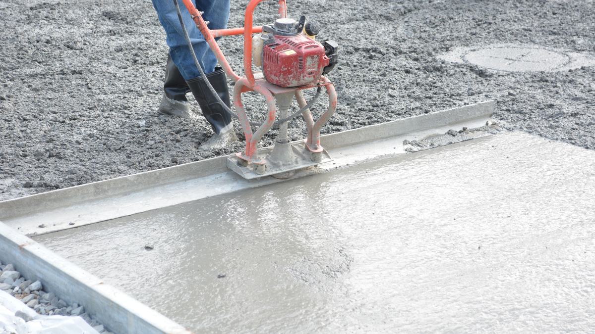 Power screed leveling a freshly poured concrete slab between steel forms