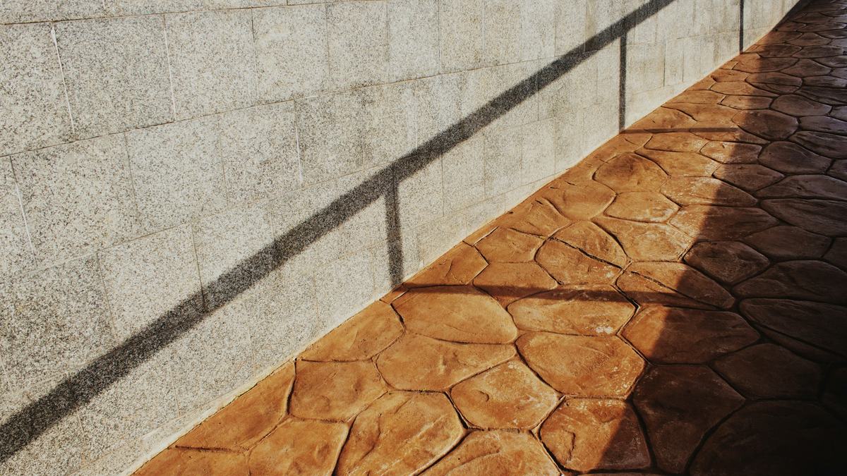 Terracotta-colored stamped concrete walkway in a flagstone pattern beside a wall